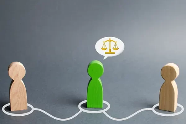 Wooden figures representing people, with a green figure in the center, connected by a line, and a speech bubble with scales indicating a discussion about fairness or mediation.